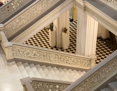 Elegant staircase with intricate railings and checkered floor in a grand interior.